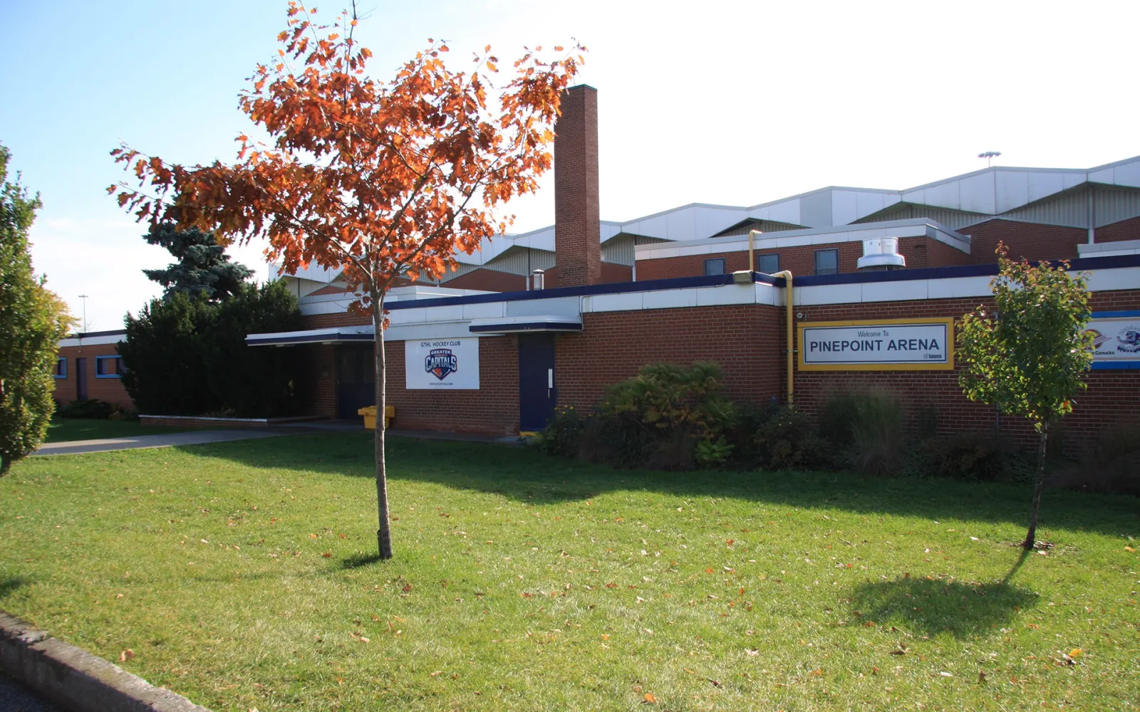 Pine Point Arena, a brick and white-roofed building with a chimney, seen across the lawn. — Pine Point Arena
