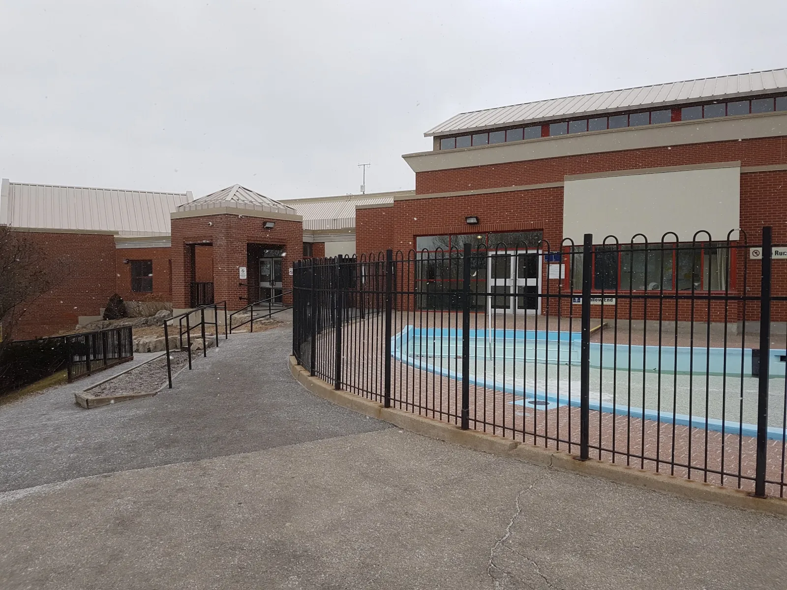 The red-brick community centre on an overcast day, with a fenced outdoor pad and a ramp leading to the entrance. — Roding Community Centre