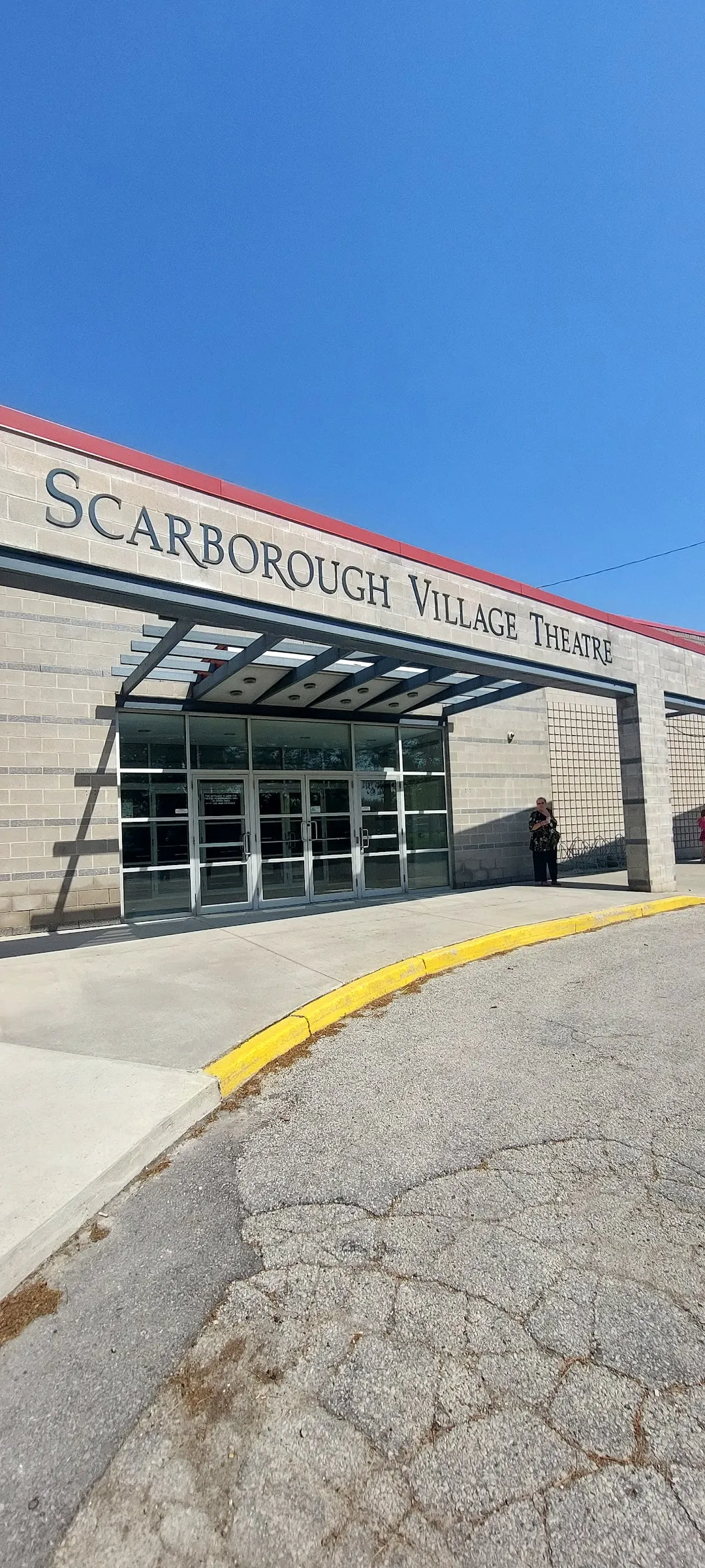 The glass entrance of Scarborough Village Recreation Centre under a canopy, with Scarborough Village Theatre lettering on the brick wall — Scarborough Village Recreation Centre