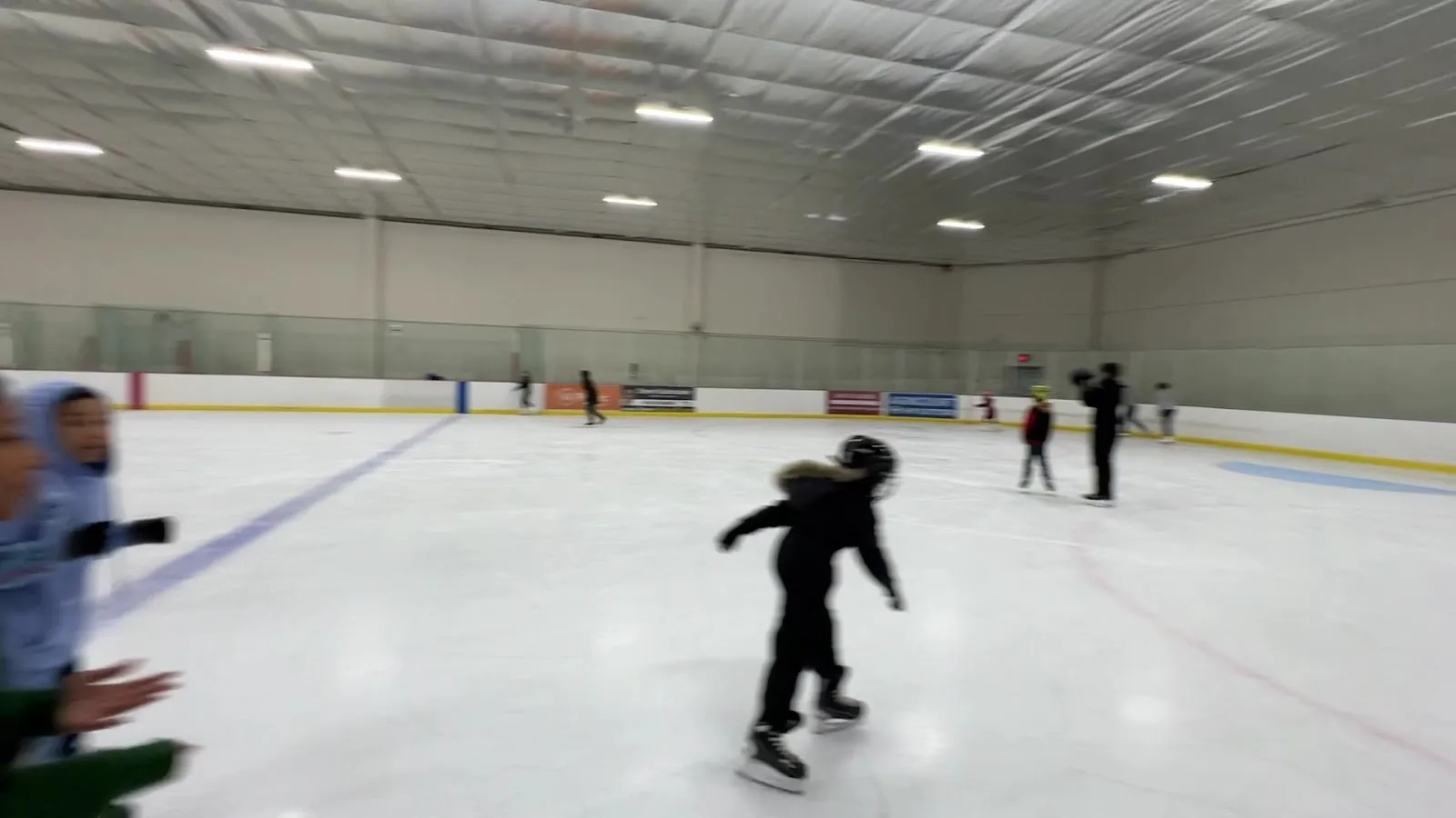 Skaters spread across a pale sheet under a long white roof with a line of fluorescent lights, a few players near the far boards. — Scarborough Village Recreation Centre