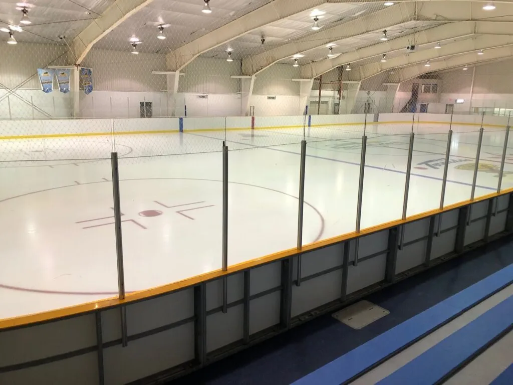 El hielo vacío visto por encima de las bardas, con mantas a lo largo de la parte superior de la pared y un techo de acero claro. — Tottenham Community & Fitness Centre