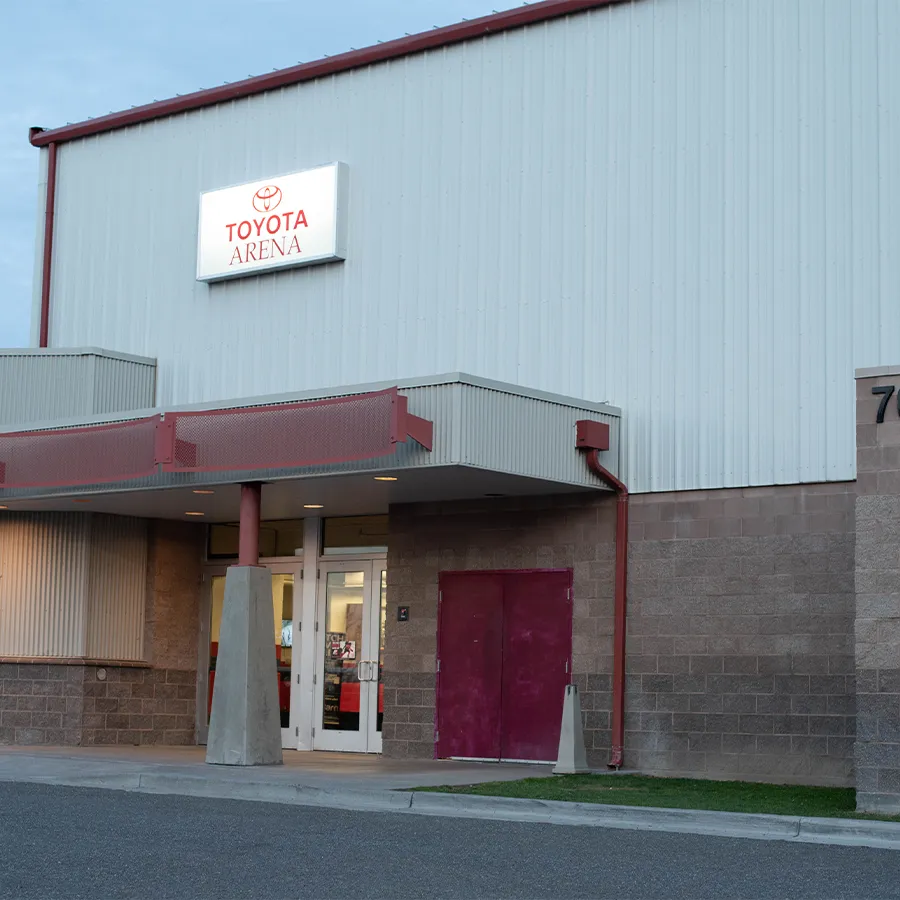Front entrance of Toyota Arena at dusk, lit "TOYOTA ARENA" sign above the canopy entrance with a red door and address numerals visible on the block wall to the right — Toyota Arena