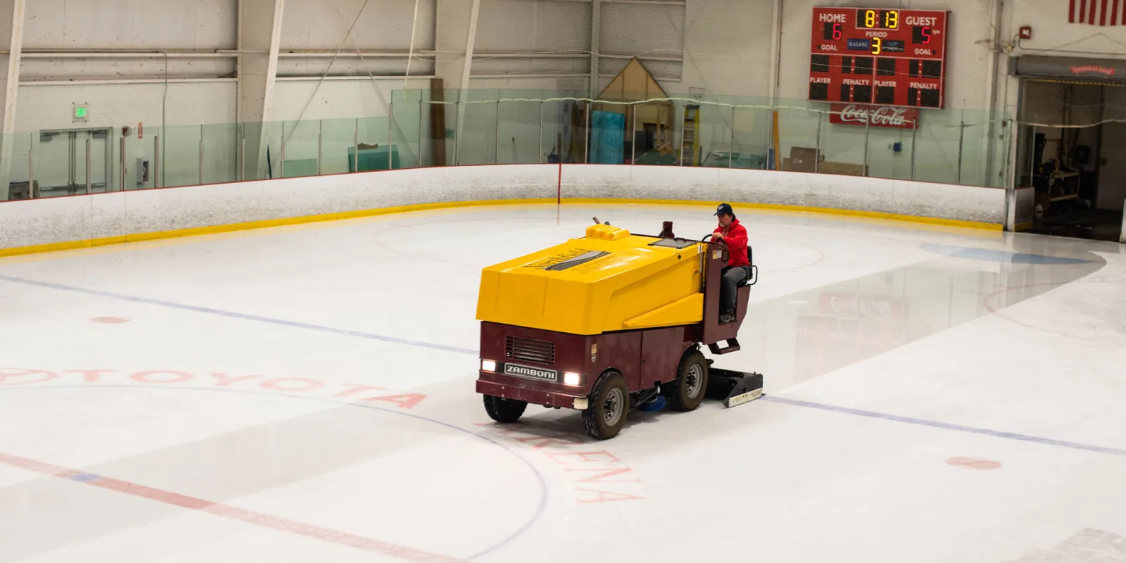 Full ice sheet inside Toyota Arena being resurfaced by a Zamboni, with "TOYOTA ARENA" painted on the ice, a scoreboard reading Coca-Cola, and the rink boards and rafters visible — Toyota Arena