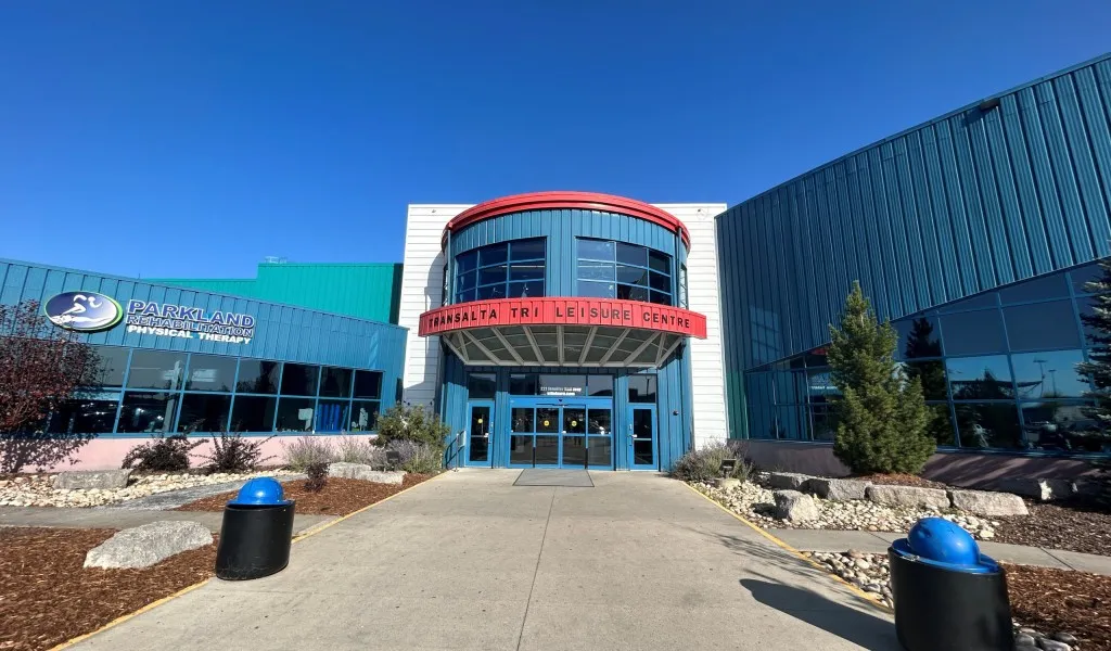 The glass entrance of the TransAlta Tri Leisure Centre with its round red-roofed entrance tower, seen from the path — TransAlta Tri Leisure Centre