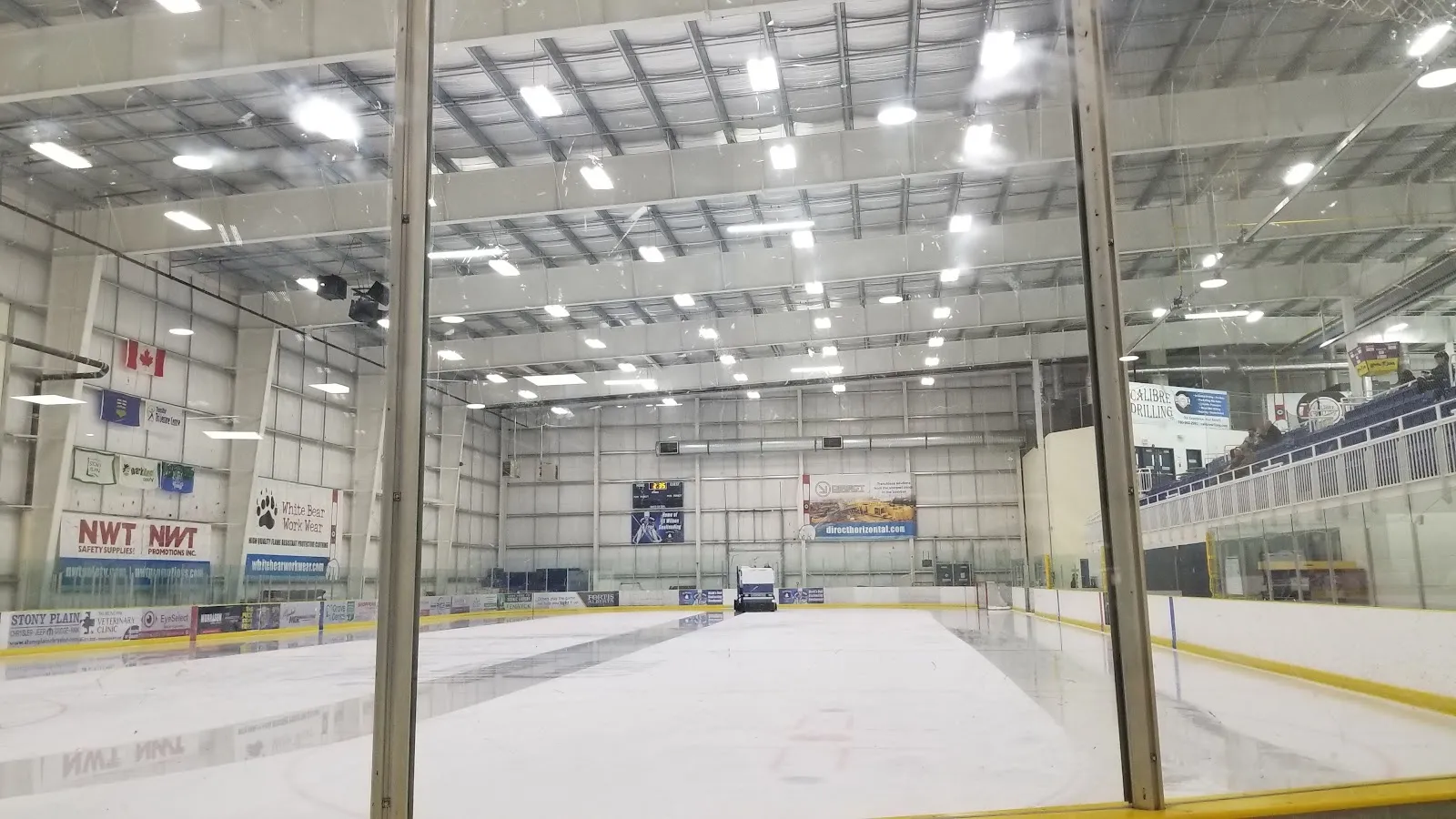 A wide empty sheet seen from the end, a blue and red line on the white ice and a banner wall and glazing on the far side. — TransAlta Tri Leisure Centre