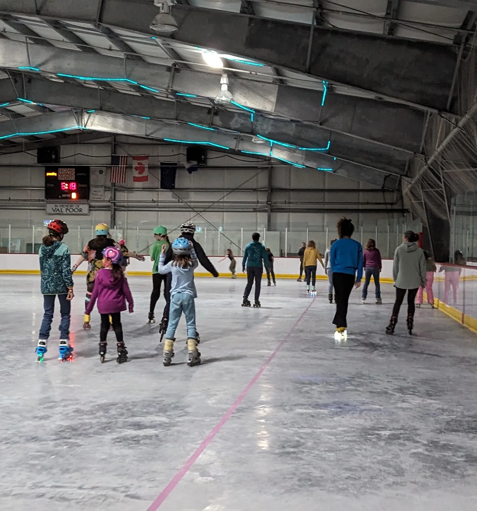 Patinadores en una sesión pública a lo largo de las vallas bajo el techo arqueado, vistos de espaldas. — Treadwell Ice Arena