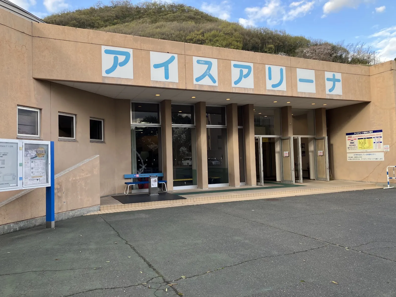 トレスタ白山アイスアリーナの入口。ガラス戸の上に青い大きなカタカナの「アイスアリーナ」の看板があり、屋根の後ろに木々の茂る丘があります — Tresta Shiroyama Ice Arena