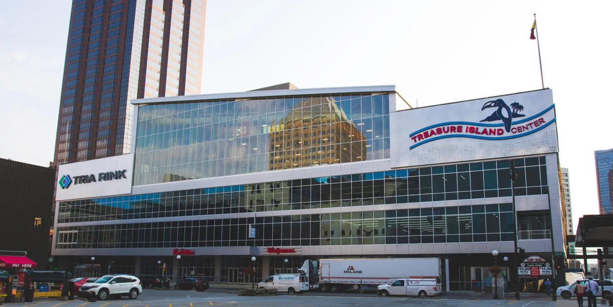Treasure Island Center from the street, with the TRIA RINK sign on the corner, the Treasure Island Center sign and the glass upper floors that hold the rink. — TRIA Rink