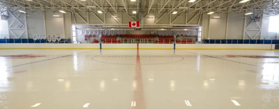 Wide view of an empty NHL-size sheet down the red centre line, with a Canadian flag and banners above the far end. — Trico Centre for Family Wellness