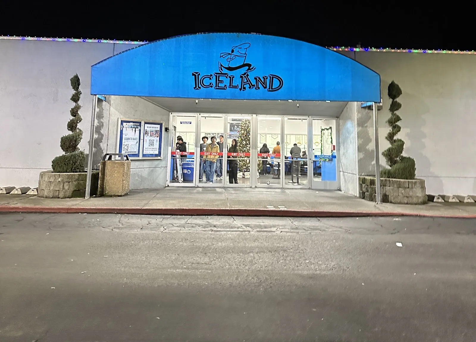 La entrada principal de la pista de Dublin de noche, bajo el toldo azul en arco de Iceland, con puertas de vidrio hacia el vestíbulo — TriValley Ice Dublin