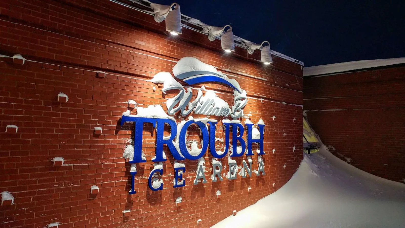 The "William B. Troubh Ice Arena" sign mounted on the building's brick exterior wall, photographed at night with snow on the roofline. — William B. Troubh Ice Arena