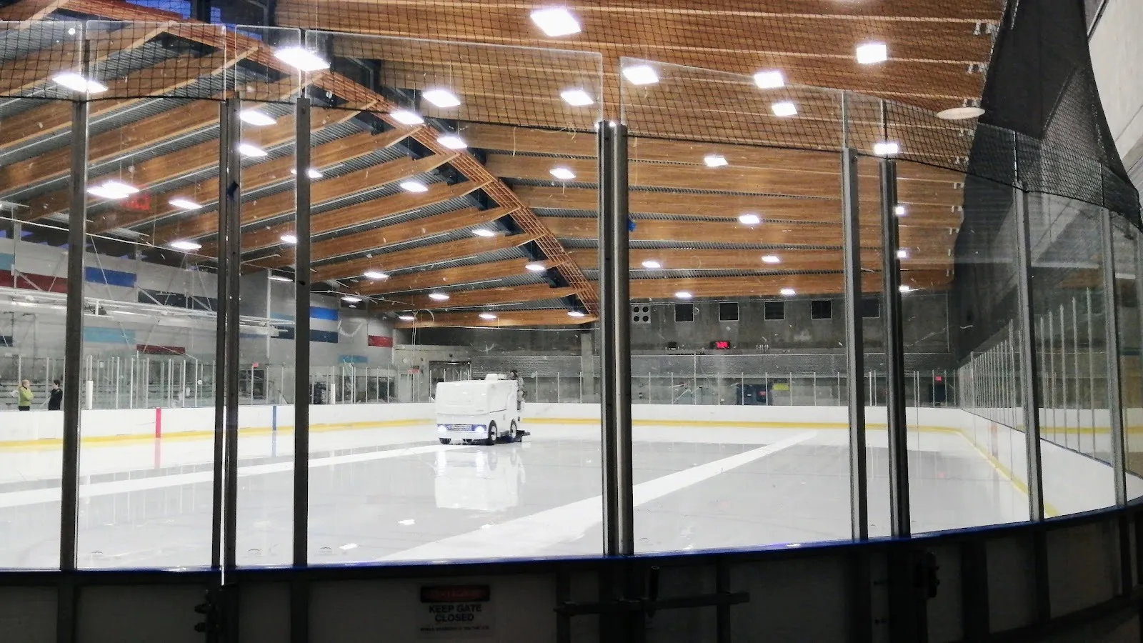La pulidora de hielo cruzando la pista de Trout Lake, vista a través del vidrio bajo las vigas curvas de madera del techo — Trout Lake Rink