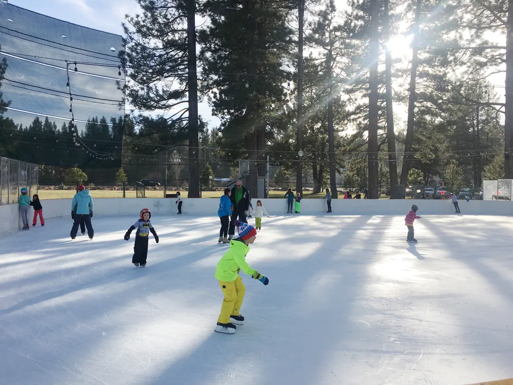 La Truckee Ice Rink en Truckee River Regional Park en un día soleado, con patinadores y pinos (foto del listado de Google Maps) — Truckee Ice Rink