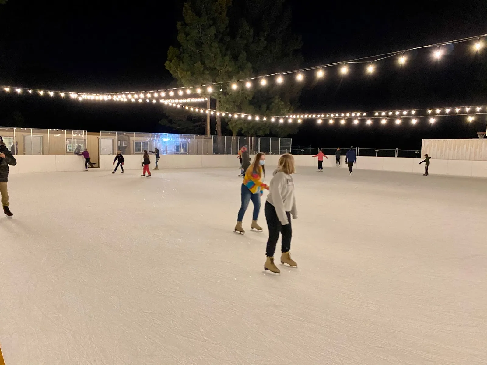 Patinadores en la Truckee Ice Rink de noche bajo tiras de luces (foto del listado de Google Maps) — Truckee Ice Rink