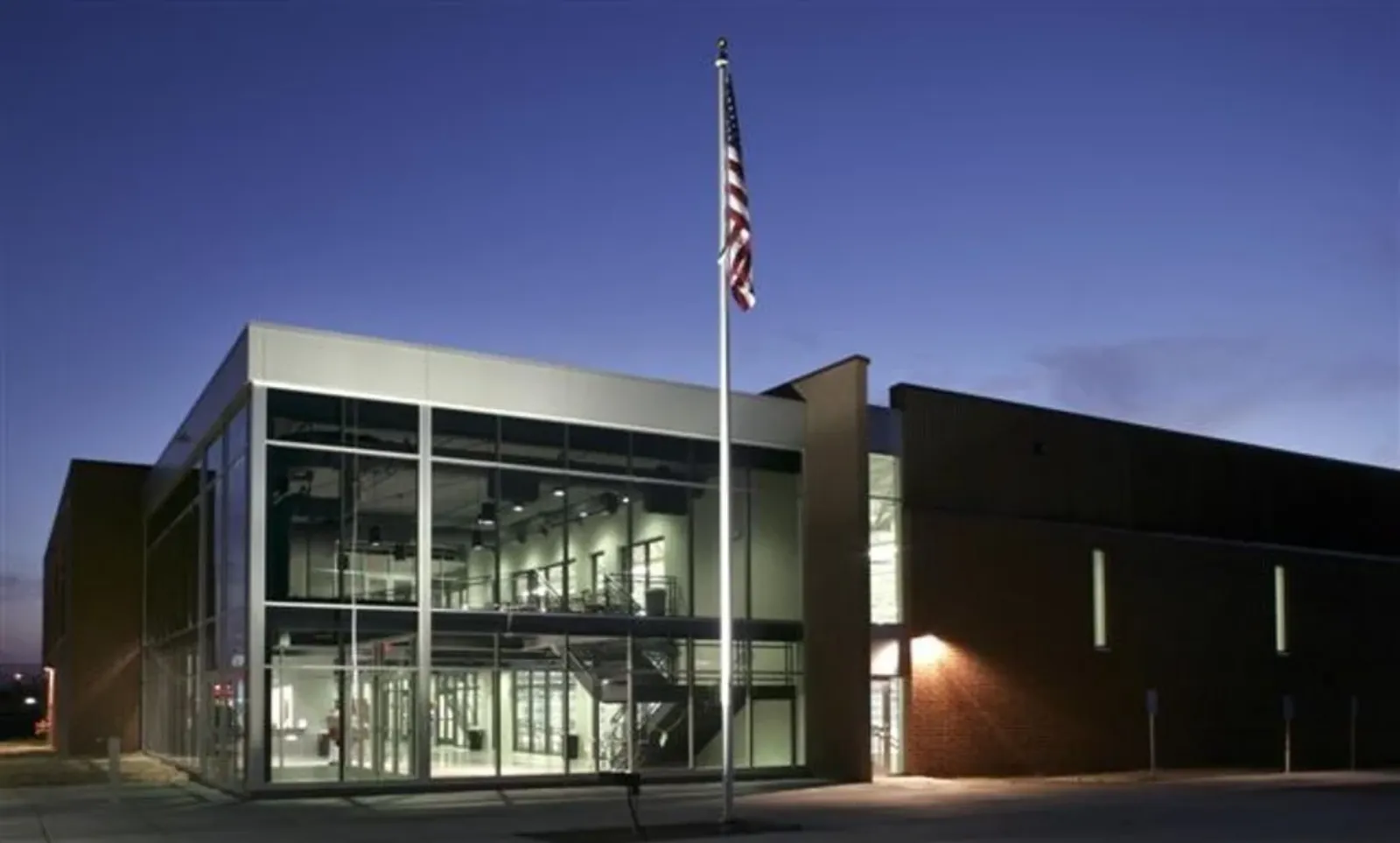 Twilight view of the TruStone Center (Rogers Activity Center): glass-fronted two-story entrance with an American flag out front, brick side wing extending to the right — TruStone Center (formerly Rogers Activity Center)