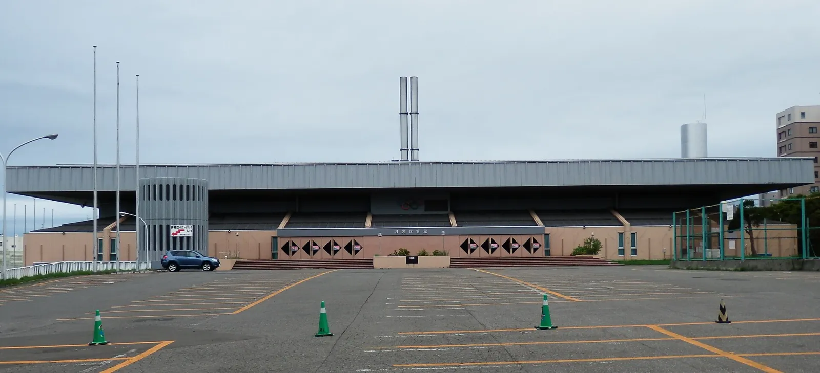 The long low front of the Tsukisamu Gymnasium, which holds the Sapporo municipal skating rink, seen from its car park — Sapporo Tsukisamu Gymnasium Skating Rink