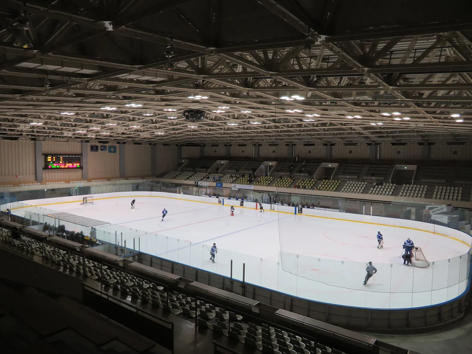 The 30 by 60 metre rink seen from the stand, with a few hockey players on the ice — Sapporo Tsukisamu Gymnasium Skating Rink