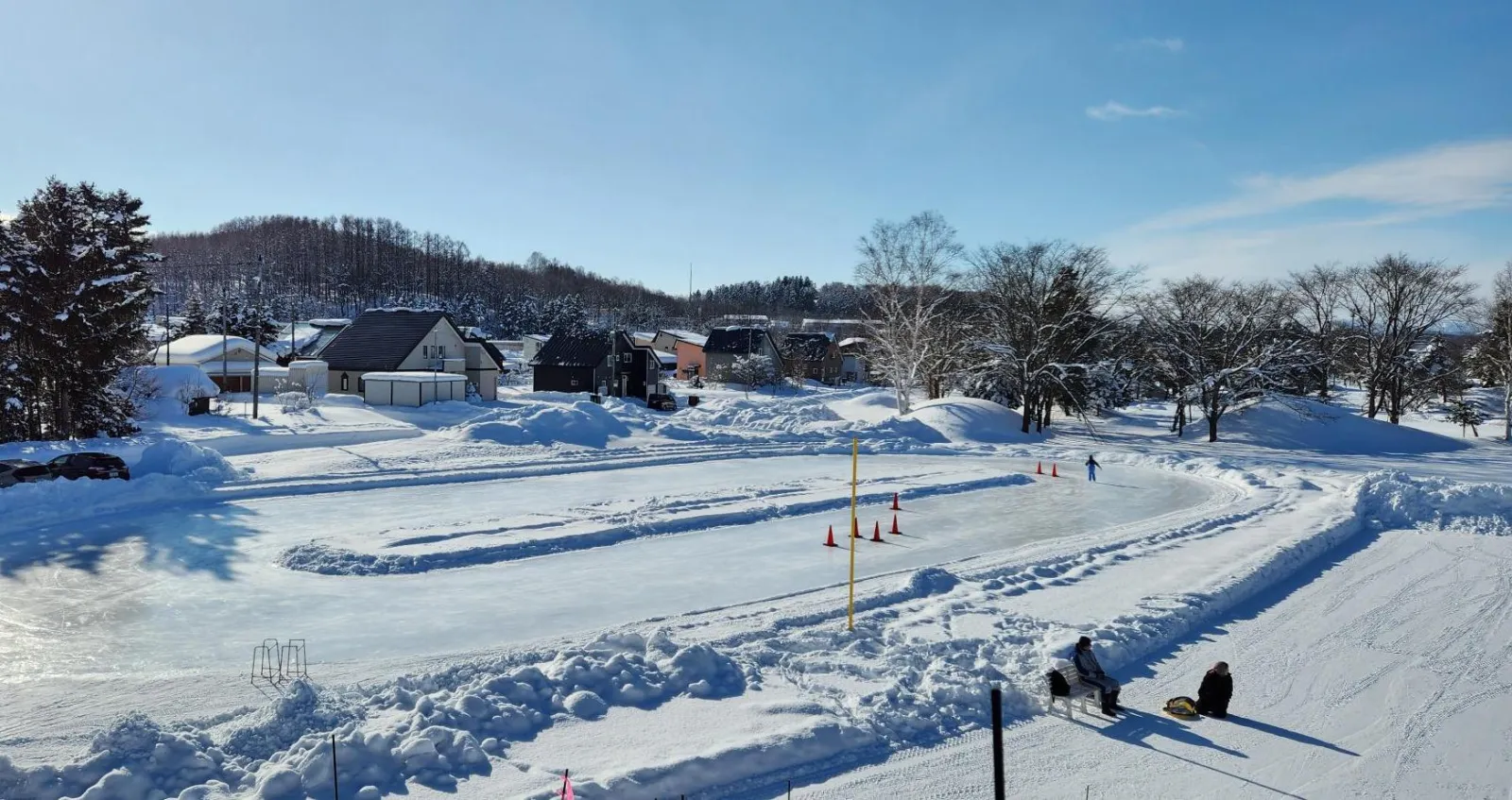 The Tsukumo skate rink in winter: the ice track laid out in Tsukumo Suigo Park, with orange cones along the lane and houses beyond. — Tsukumo Skate Rink