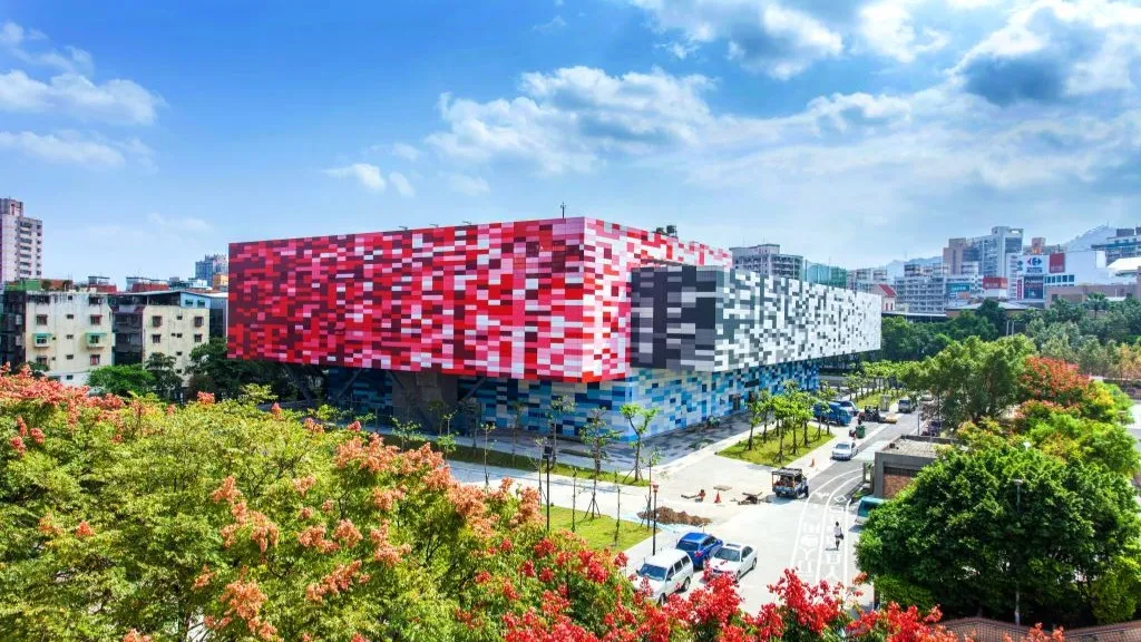 The pink, red and white mosaic facade of Tucheng Civil Sports Center, which houses the ice palace on its third floor, seen from above across the road and the trees. — Tucheng Ice Palace (New Taipei)