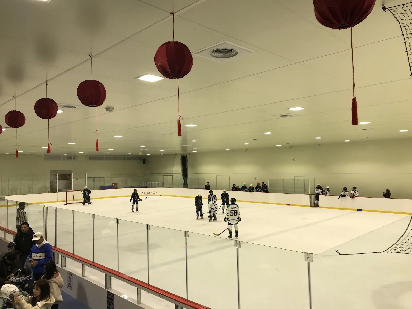 Skaters on the ice of the Tucheng Sports Center ice palace under red lanterns, with the glass and the hall wall behind. — Tucheng Ice Palace (New Taipei)