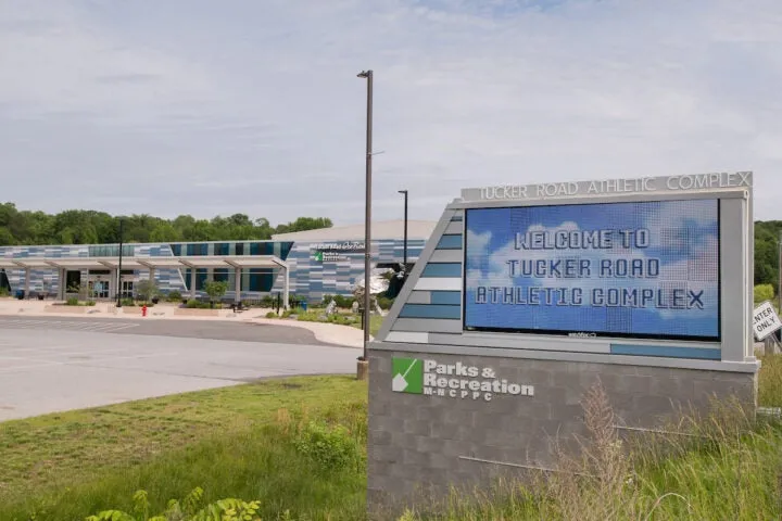Entrada principal del edificio del Tucker Road Athletic Complex, con un letrero monumental iluminado que dice "Welcome to Tucker Road Athletic Complex" y el logotipo de Prince George's Parks & Recreation, visto desde el estacionamiento. — Tucker Road Ice Rink