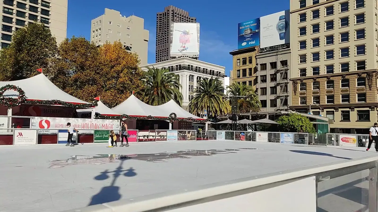 The open-air sheet on the plaza in daylight, with the rink's white canopies and holiday garlands along the far side and the surrounding Union Square buildings behind. — Union Square Ice Rink