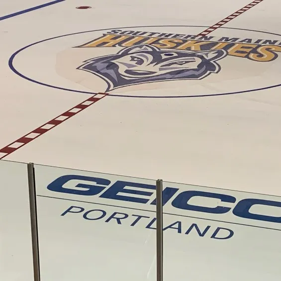 The Southern Maine Huskies logo at centre ice behind the boards at the USM Ice Arena — USM Ice Arena