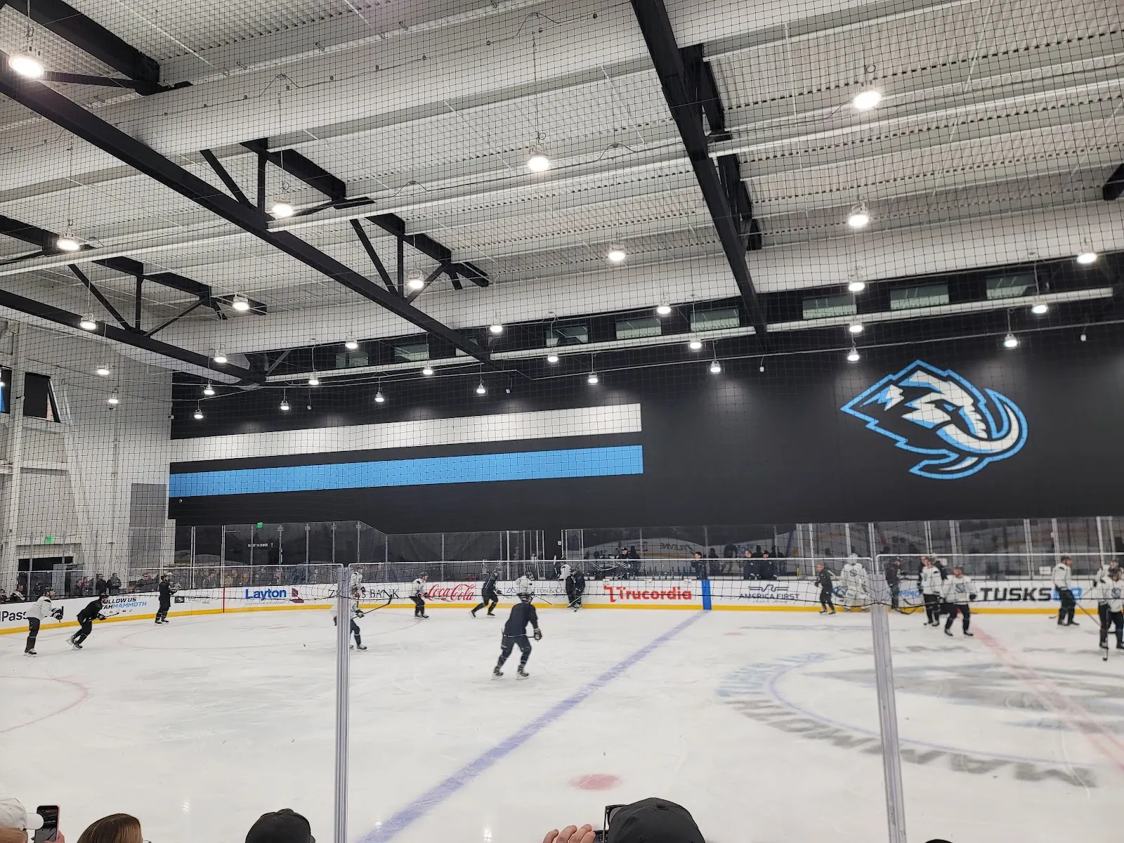 La pista principal del Utah Mammoth Ice Center durante una práctica, con el logotipo de Mammoth en un largo mural negro sobre las vallas del fondo. — Utah Mammoth Ice Center