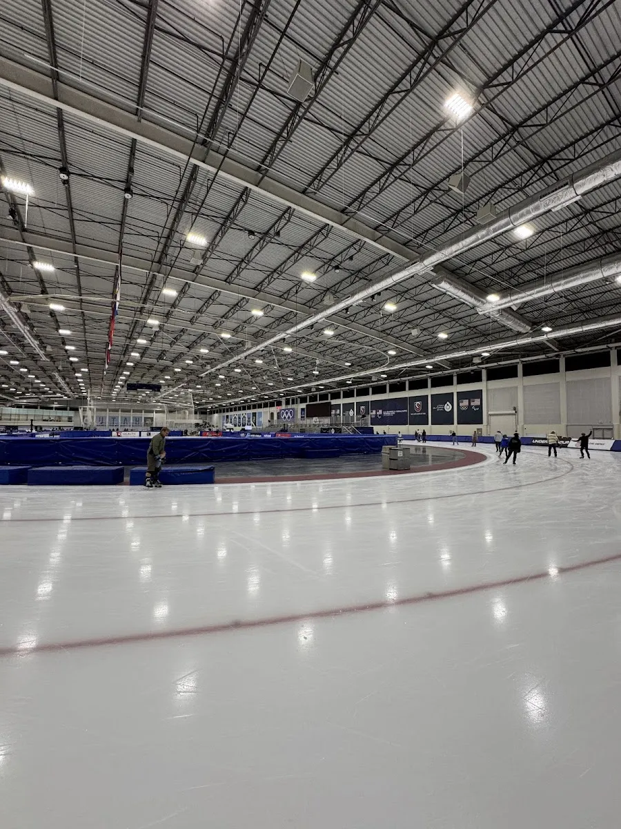The 400-meter speed skating track curving away under the arena roof, with a few skaters on the far straight. — Utah Olympic Oval