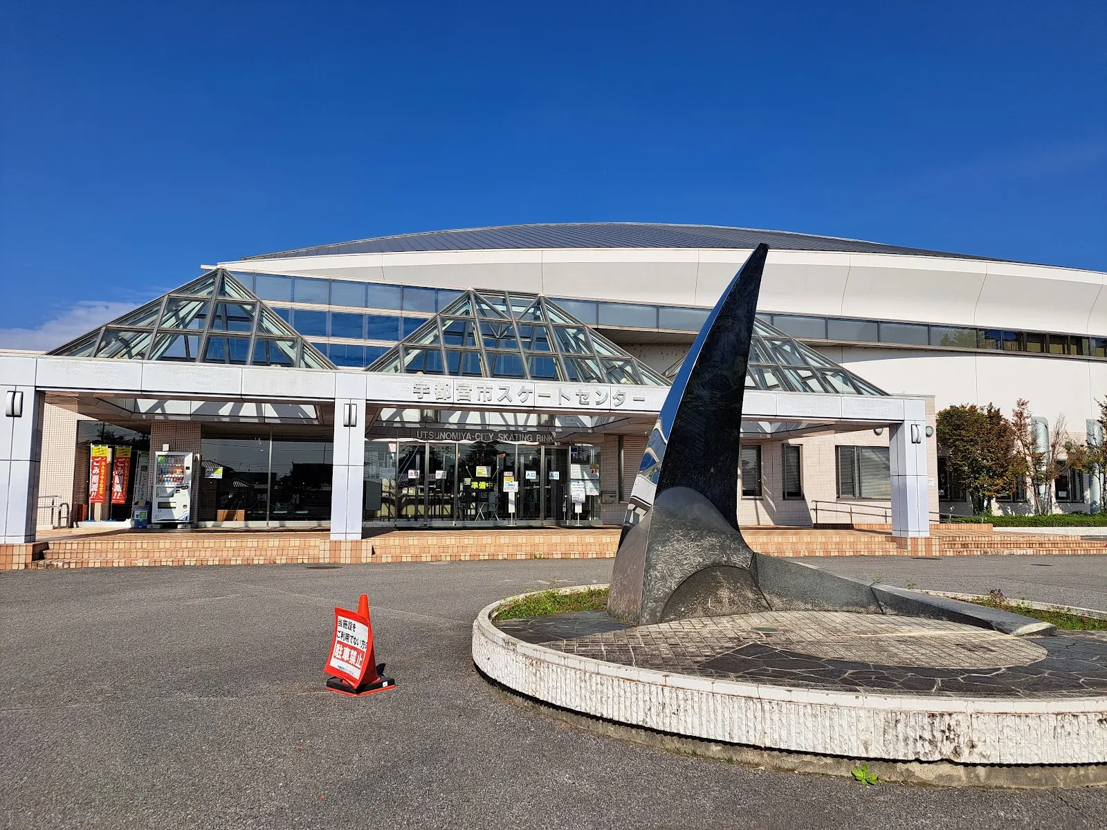 The entrance of the Utsunomiya City Skate Center under its glass roof, with the name over the door and a sculpture in the forecourt — Utsunomiya City Skate Center