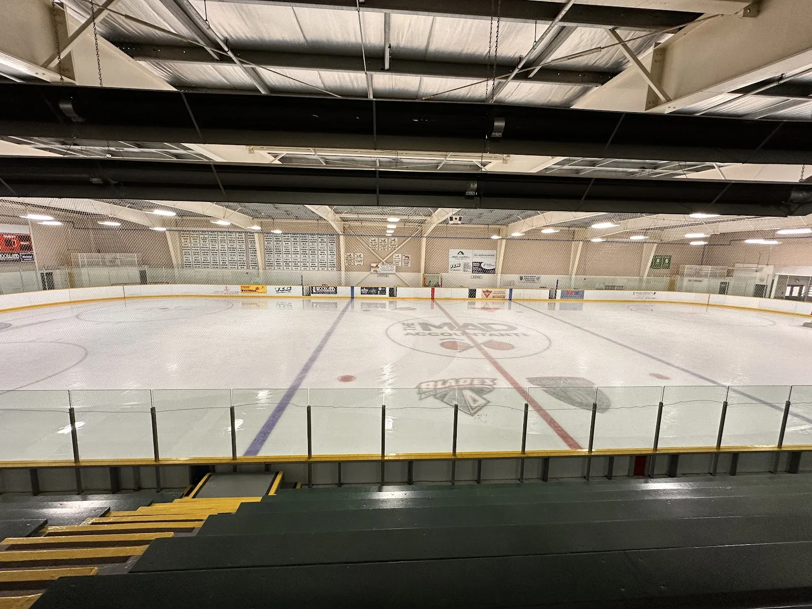 An empty pad seen over the glass from the stands, with the centre-ice logo and sponsor boards on the far side. — Uxbridge Arena and Community Centre