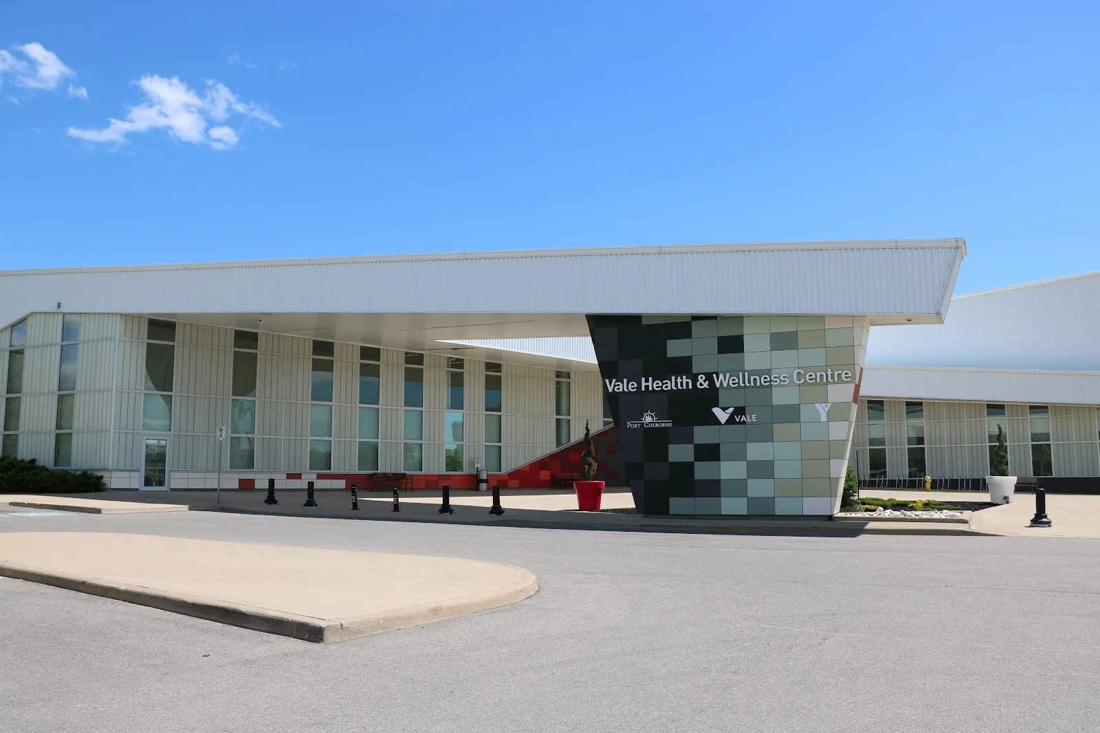 The centre's long white front with a wide canopy and a tiled pillar carrying the Vale Health & Wellness Centre sign, seen across the drop-off loop. — Vale Health & Wellness Centre