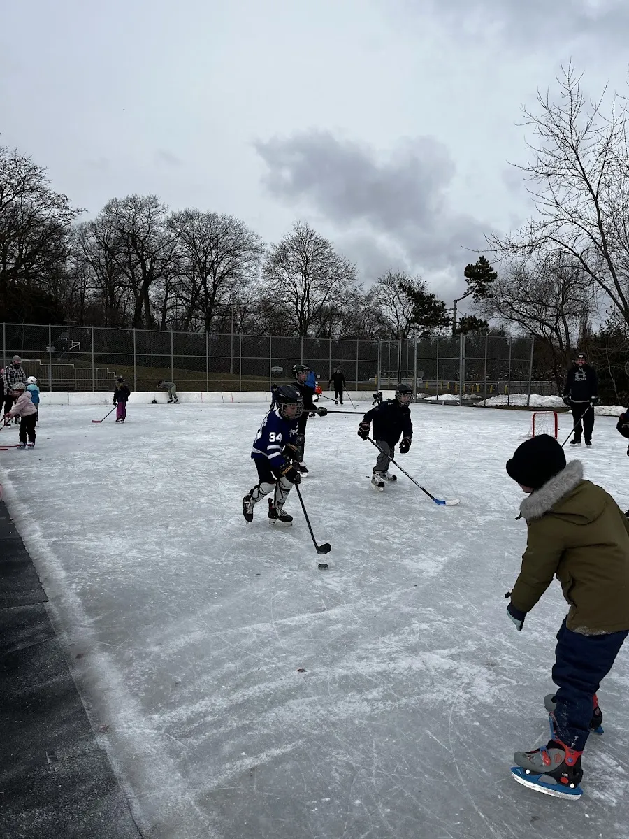 Un juego de hockey libre en la pista al aire libre de Valleyfield Park, con vallas, cerca y árboles del parque detrás — Valleyfield Park Outdoor Ice Rink