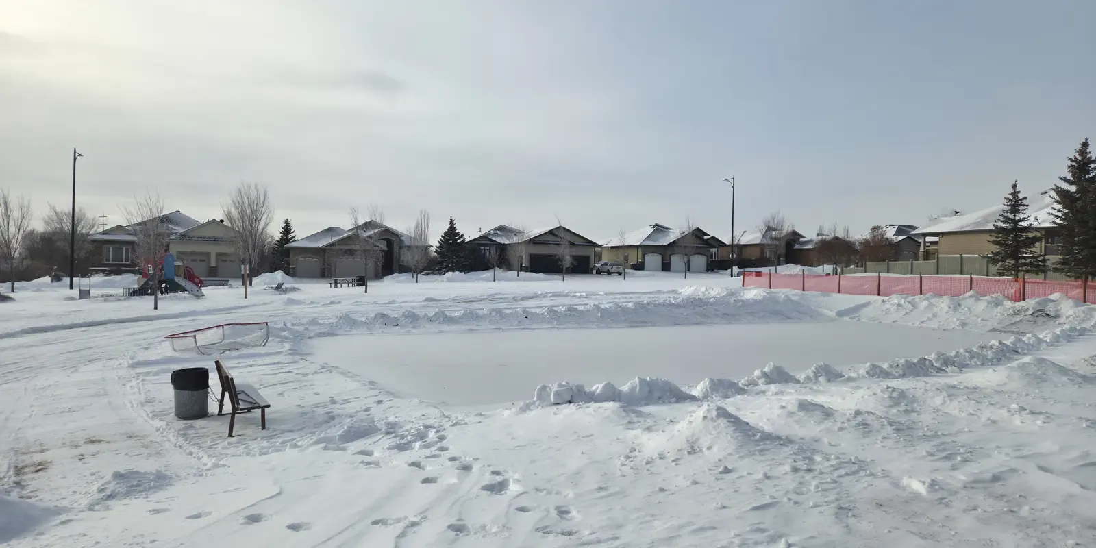 The snow-edged Valleyview South rink in Camrose in winter light, with a goal on the ice and houses and bare trees along the far edge. — Valleyview South Rink