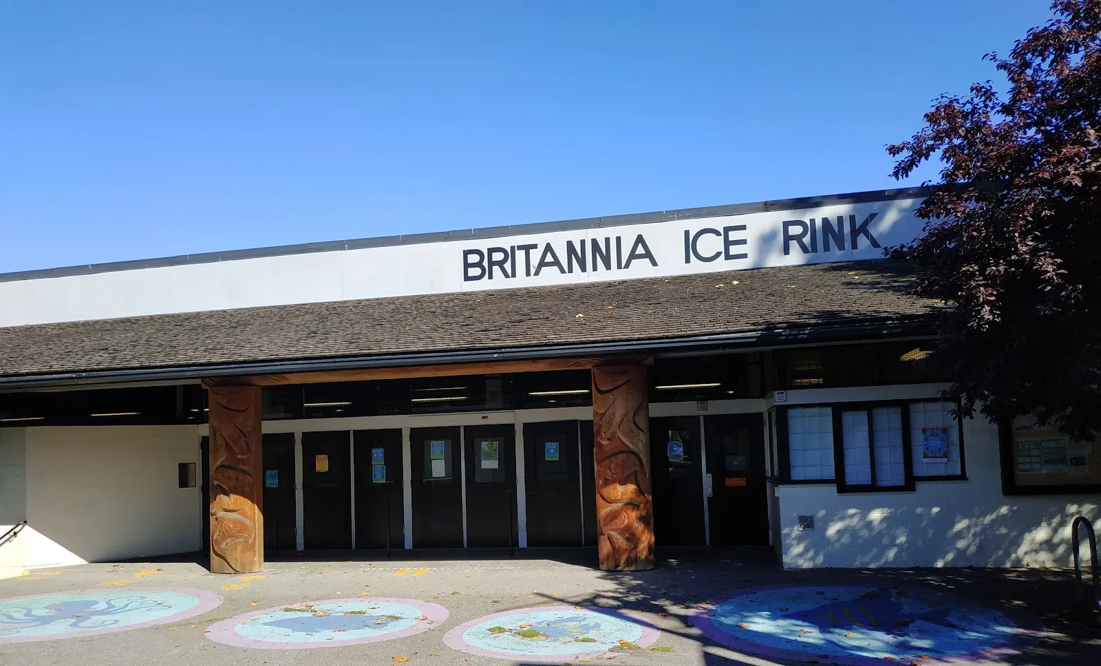 Front entrance of the Britannia Ice Rink building, with a large 'BRITANNIA ICE RINK' sign along the roofline and two carved wooden entrance posts flanking the doors. — Britannia Rink