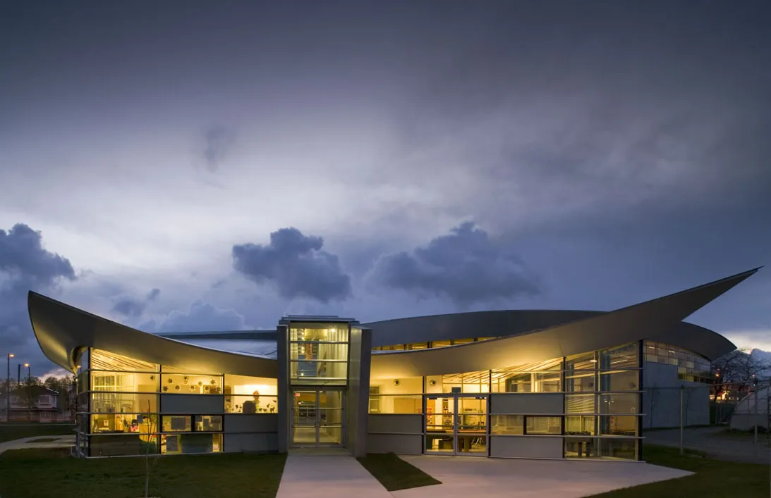 Dusk exterior of the Sunset Community Centre, home of Sunset Rink, its sweeping curved roof lit from inside. — Sunset Rink