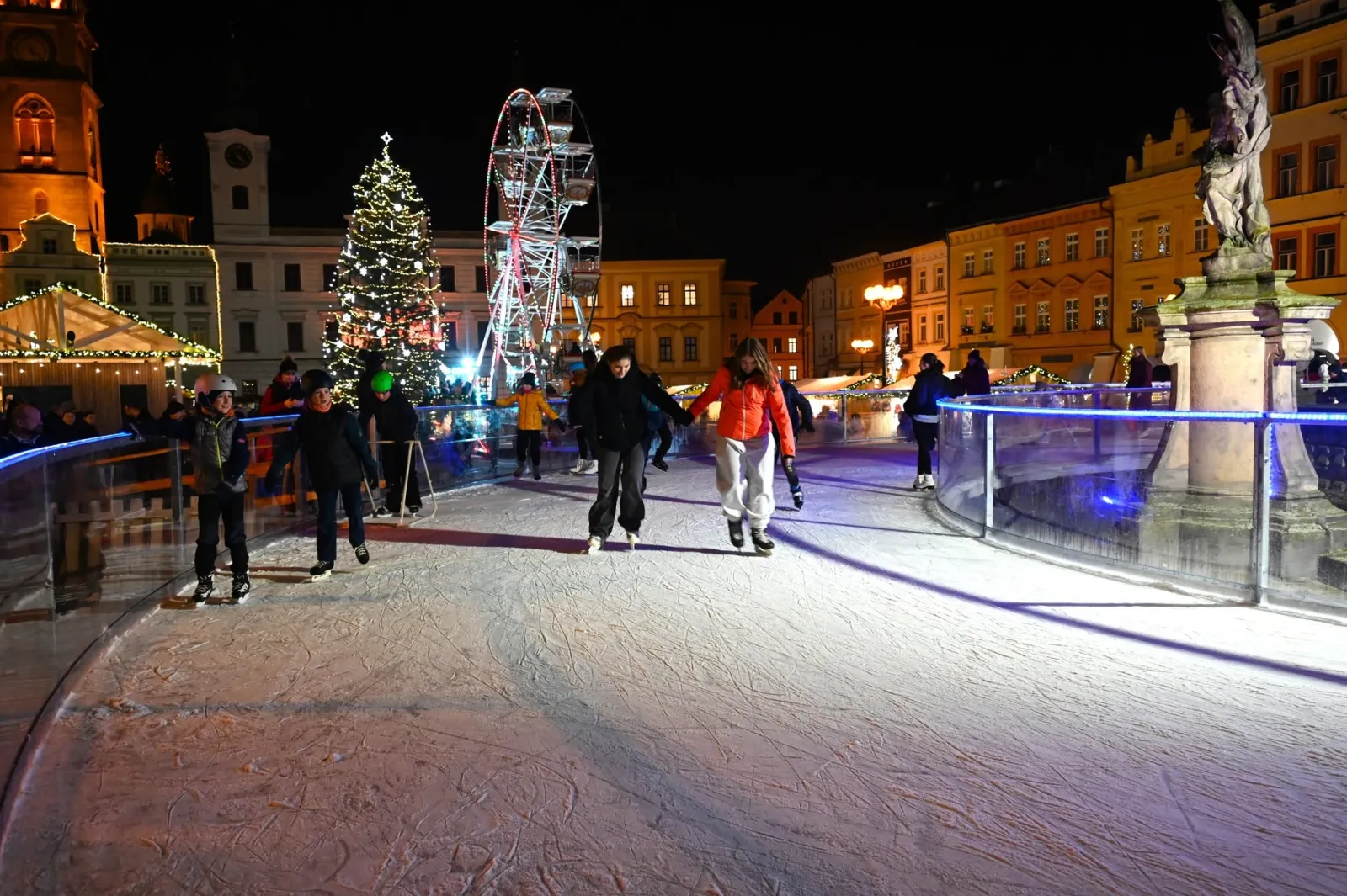 Skaters on the lit Christmas rink in the centre of Hradec Králové at night, with a Christmas tree and a Ferris wheel in the background. — Vánoční kluziště Hradec Králové