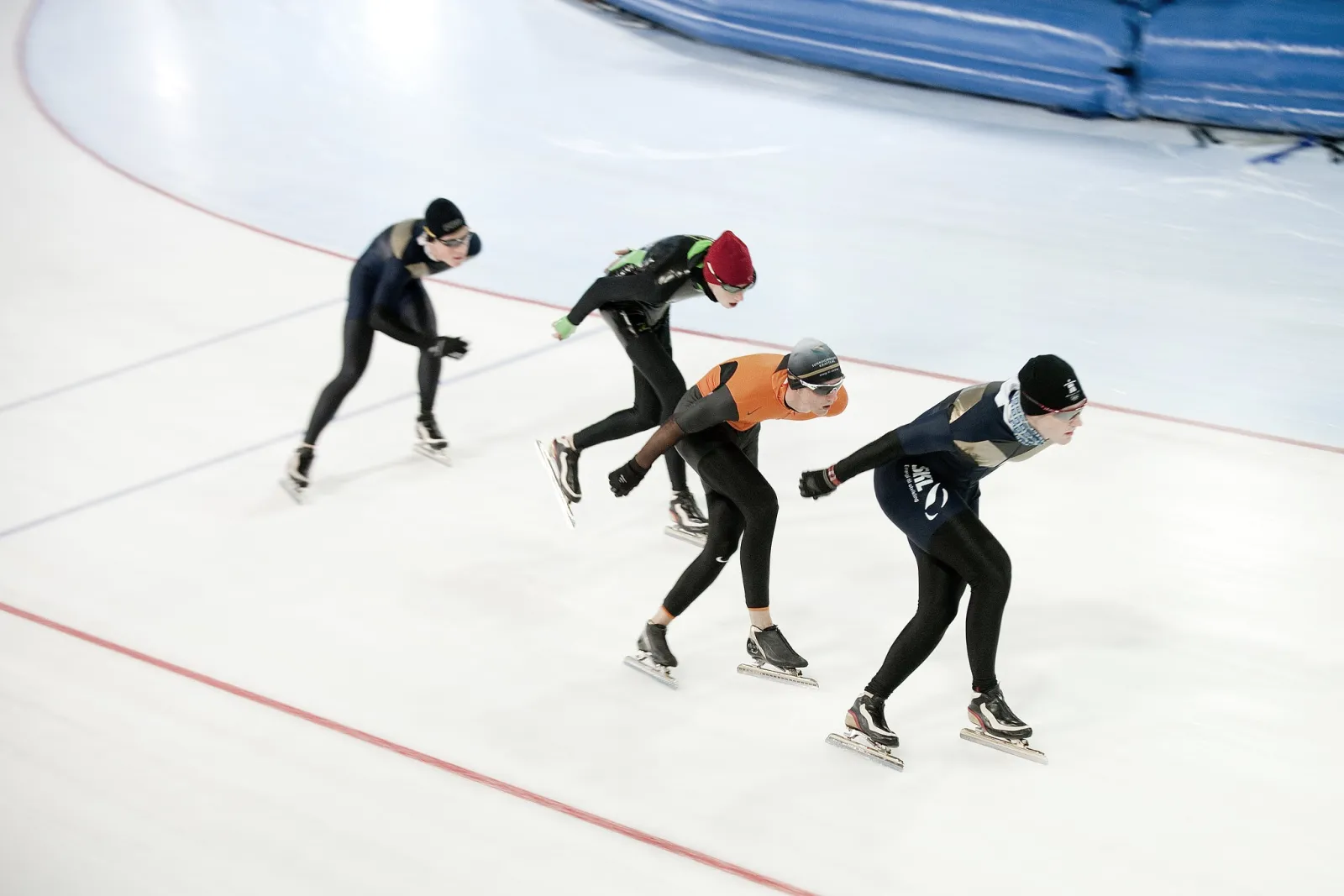 Four speed skaters in a line gliding across the ice of the Sørmarka arena. — Vår Energi Arena Sørmarka
