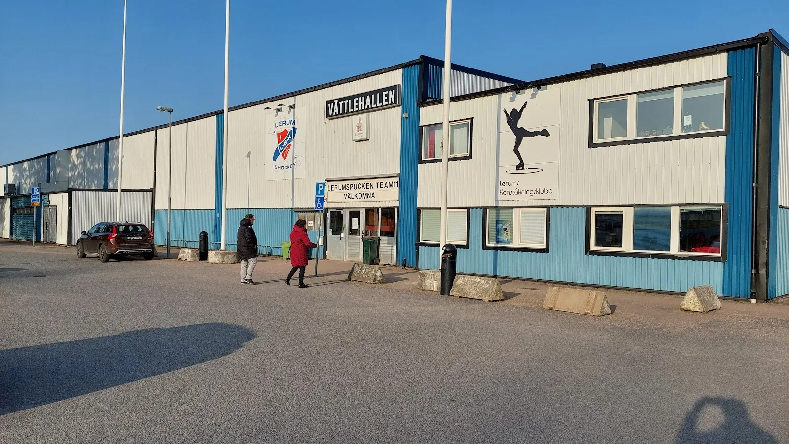 Framsidan av den blå och vita hallen med skylten Vättlehallen ovanför entrén. – Vättlehallen ishall