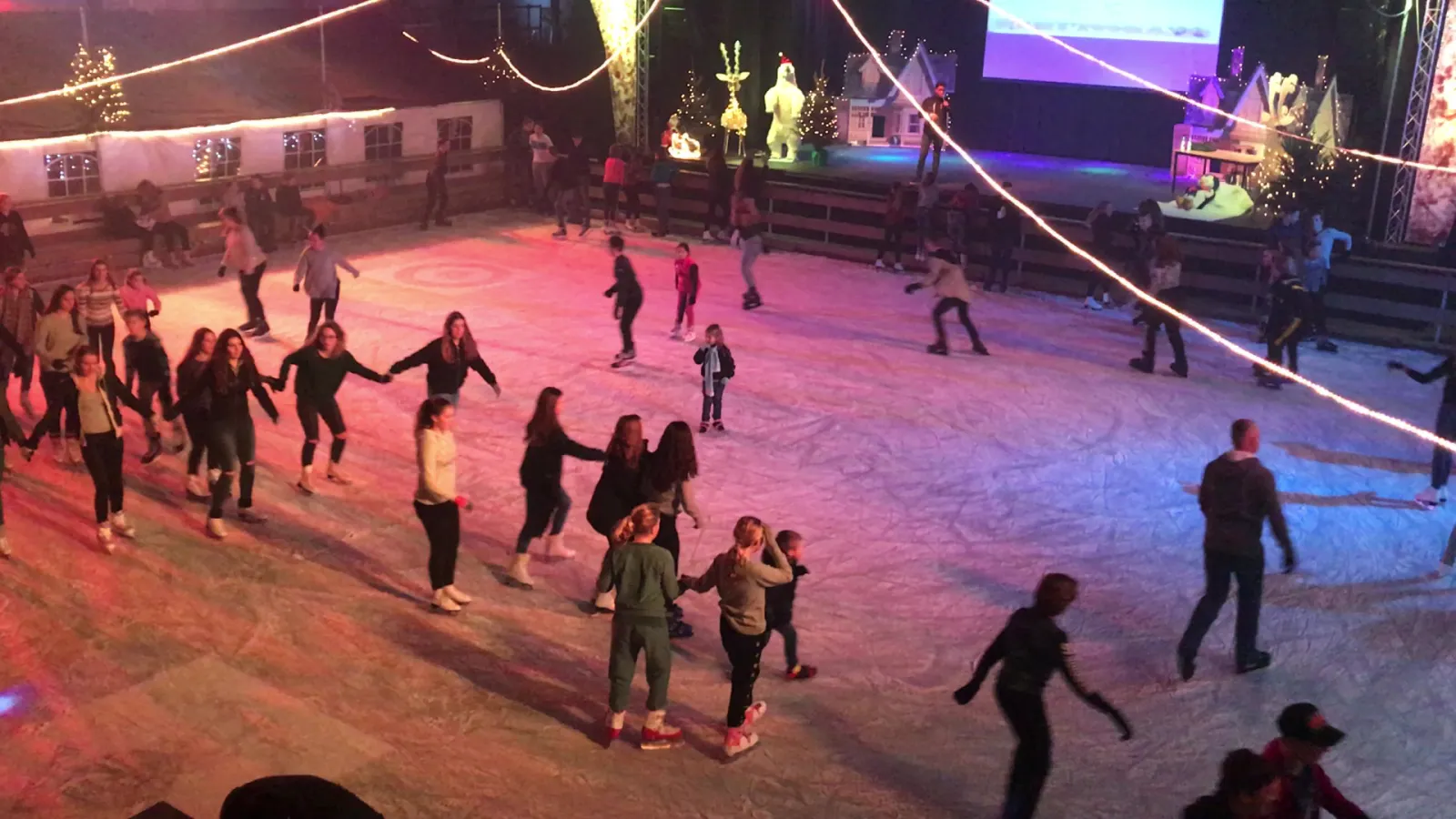 Skaters across the lit ice of 't Veerse IJsplein in the evening, seen from the side of the rink — 't Veerse IJsplein (Heereplein, Raamsdonksveer)