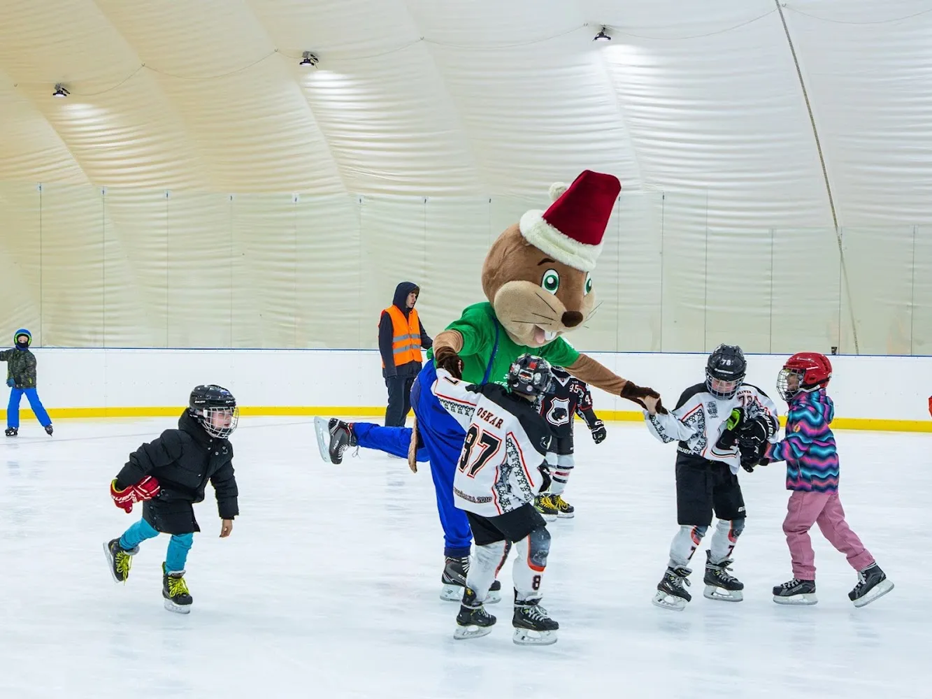 The inflatable hall's ice with children in hockey jerseys playing with the operator's mascot at a practice session; the people are playing, not posing for the camera. — Veolia Aréna Draždiak