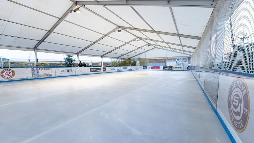 La glace vide de la patinoire Versoix on Ice sous sa tente blanche, avec les bandes et un long filet sur un côté. — Versoix on Ice (Terrain du Verger, Lachenal)