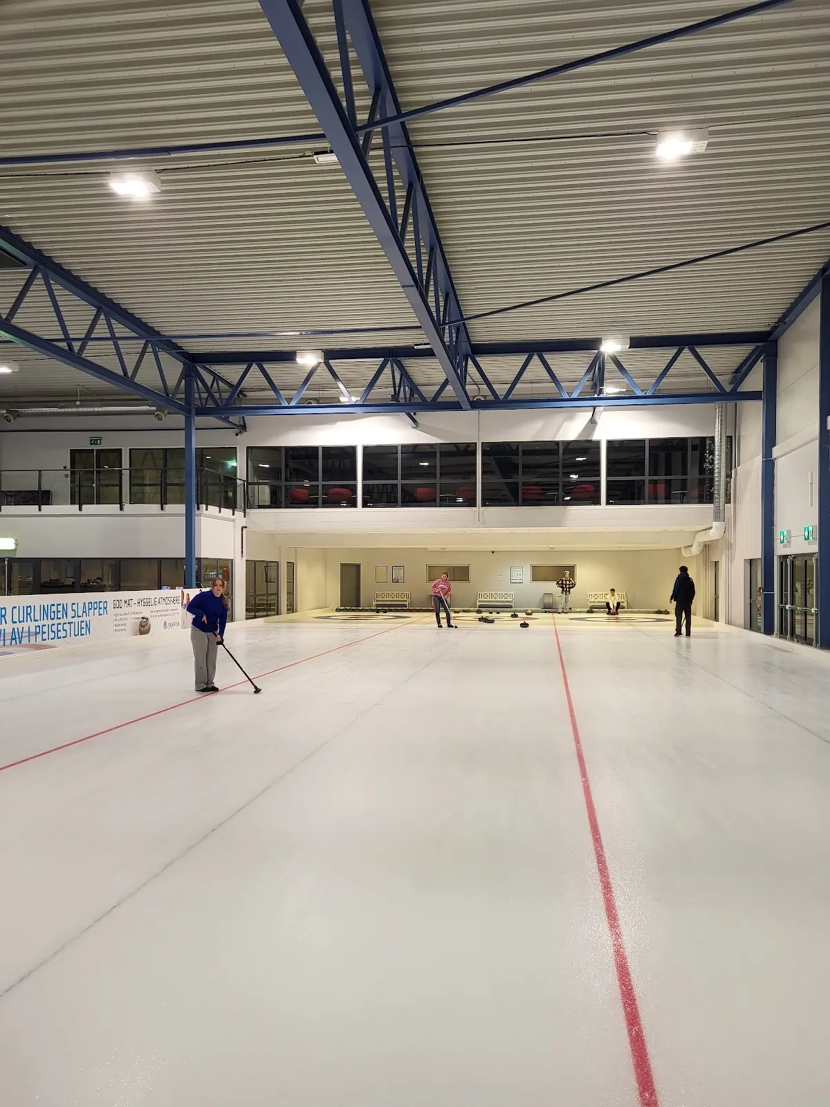The ice sheet inside Vestkanten Ishall (Iskanten) under a steel-truss roof, with a red line down the ice and a few skaters far away. — Vestkanten Ishall (Iskanten)