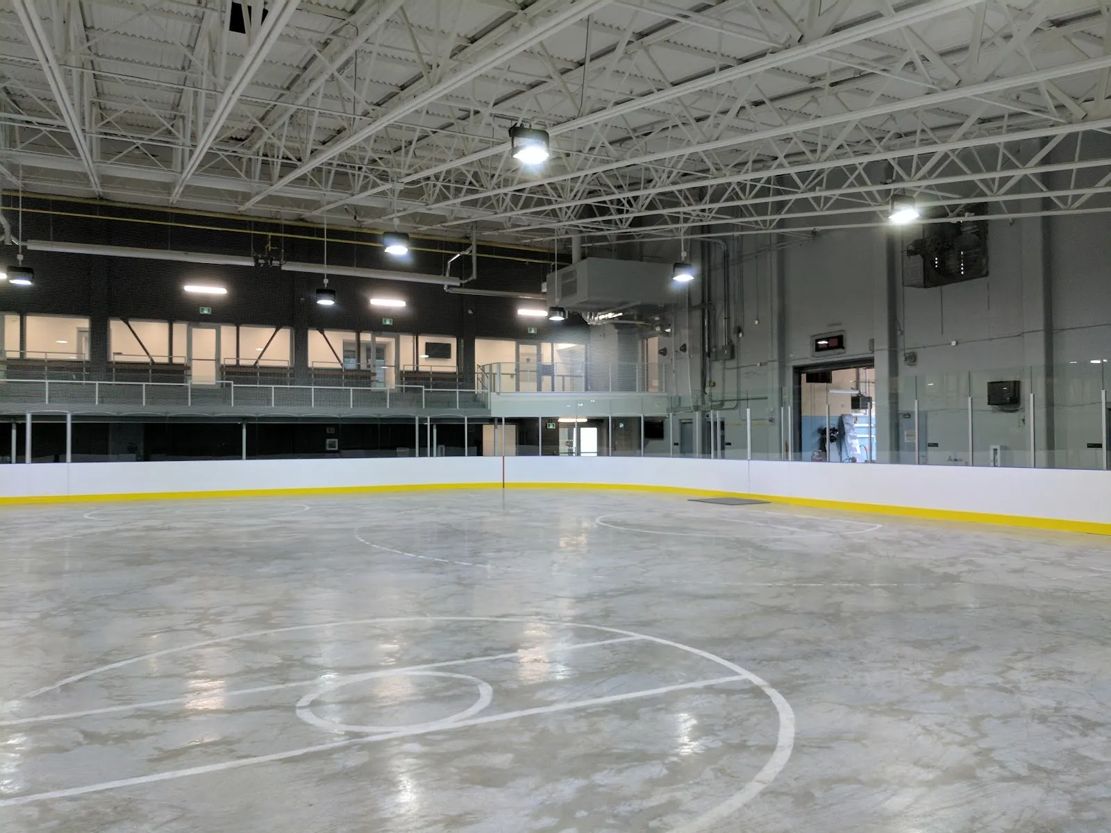 La pista vacía bajo un techo de acero blanco, con el pasillo superior y ventanas a lo largo del lado lejano. — Victoria Road Recreation Centre