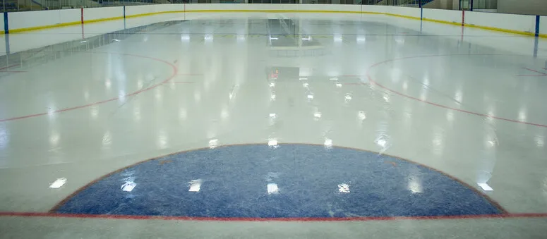 The empty Viking Carena ice surface, with a large blue painted semicircle in the foreground and the boards and glass beyond. — Viking Carena Complex