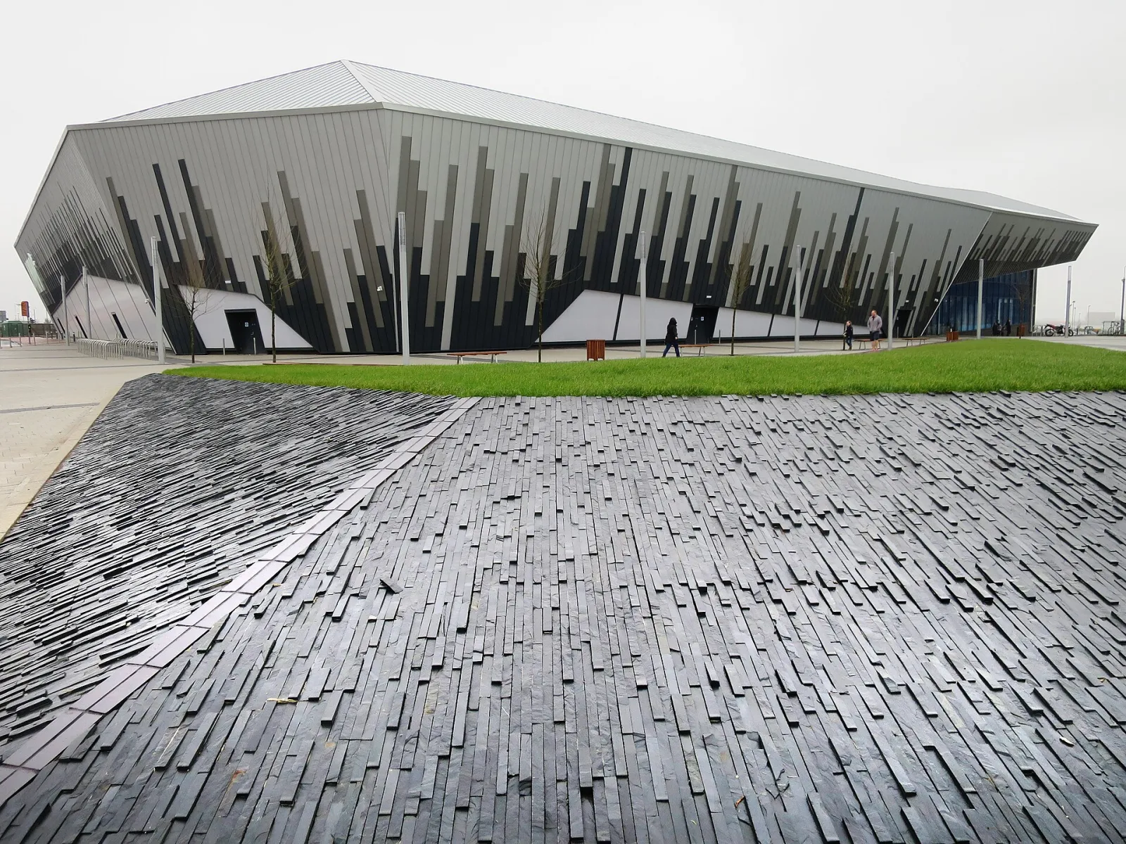 The arena's angular grey and black cladding seen across the slate-paved forecourt, photographed in February 2016 as Ice Arena Wales. — Vindico Arena