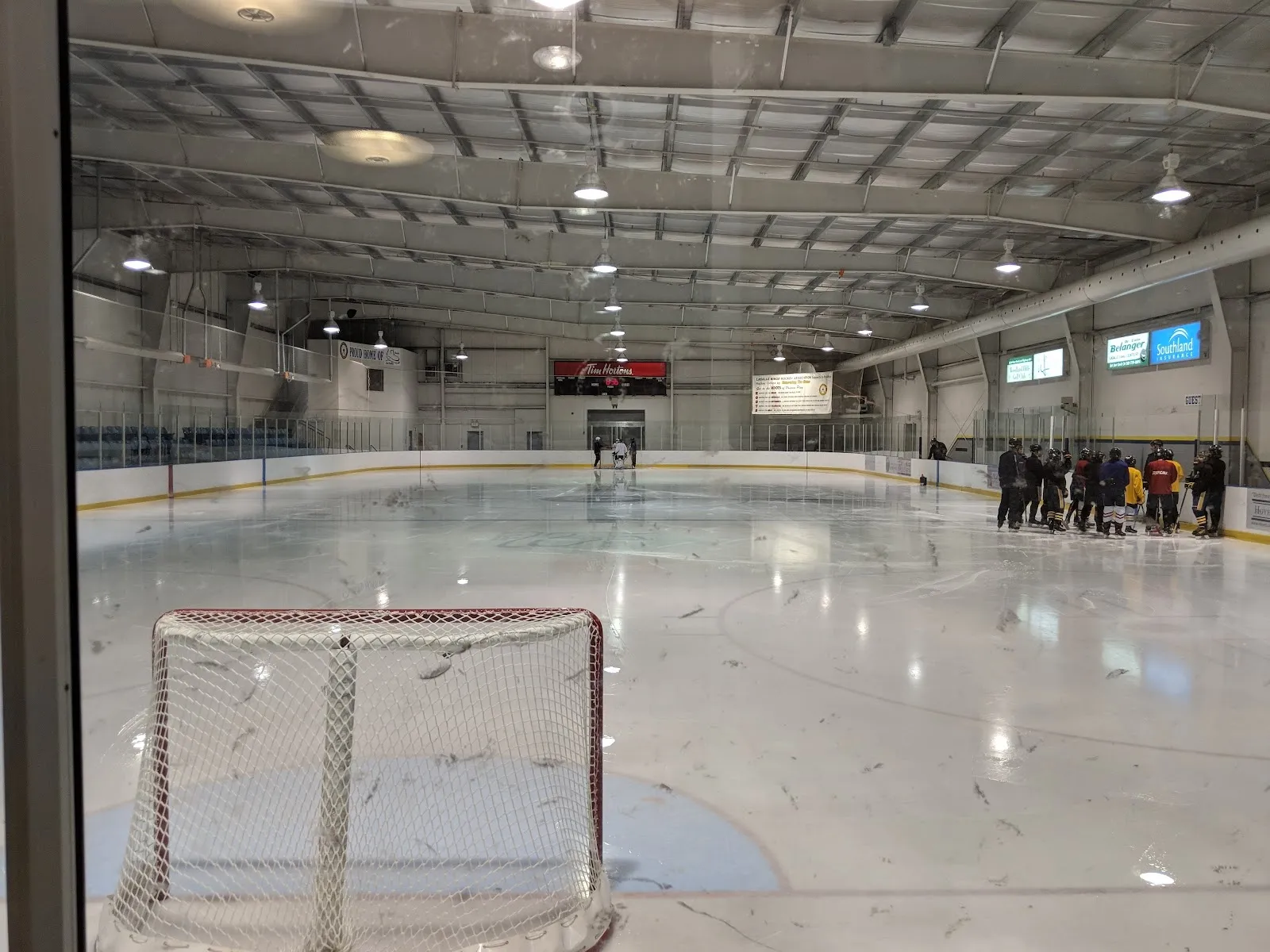 An empty sheet seen through the glass with a goal in the foreground, white ice and a far wall of glazing under a steel-trussed roof. — Vollmer Complex