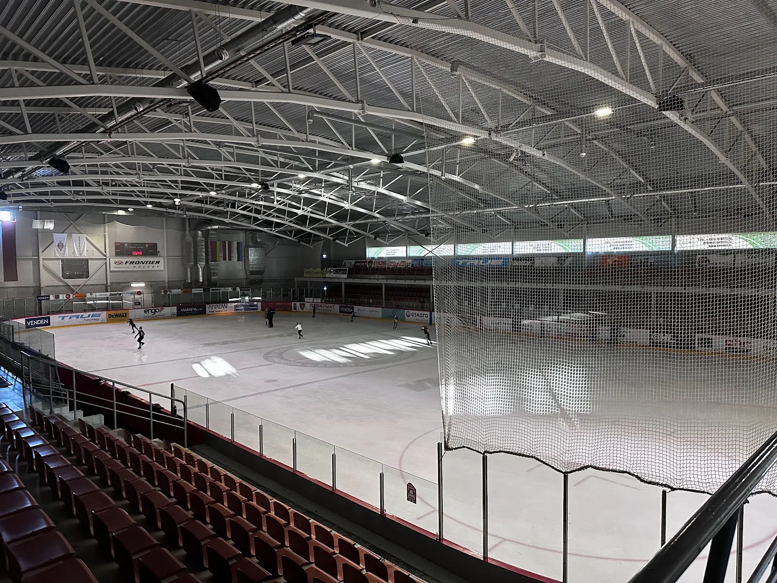 The ice hall seen from the seating rows, with the boards, the roof arches and a few skaters on the ice. — Volvo sporta centrs