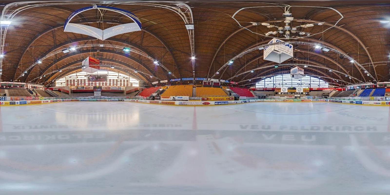 Das leere Eis der Vorarlberghalle unter dem gewölbten Holzdach, mit Banden und Zuschauerrängen rings um die Fläche. – Vorarlberghalle Feldkirch