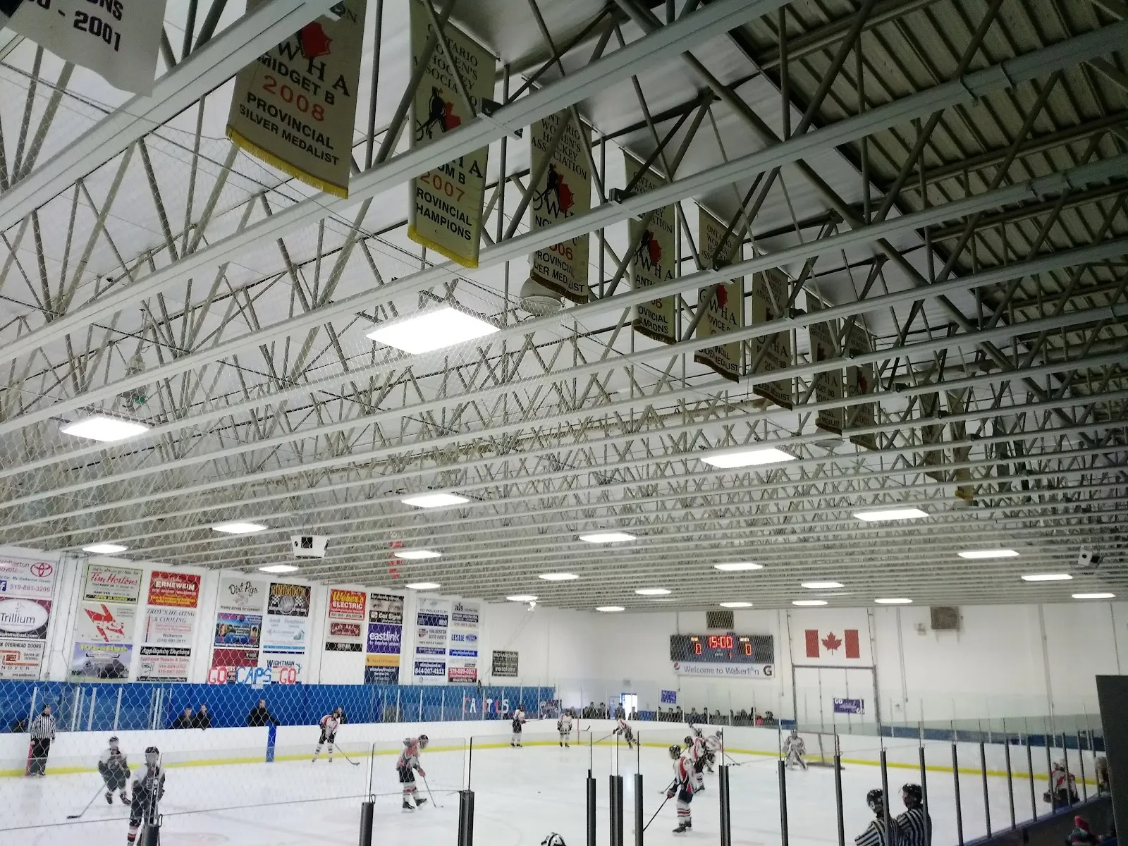 A game on the ice at the Walkerton Community Centre, with provincial championship banners on the wall and the scoreboard above the far boards. — Walkerton Community Centre